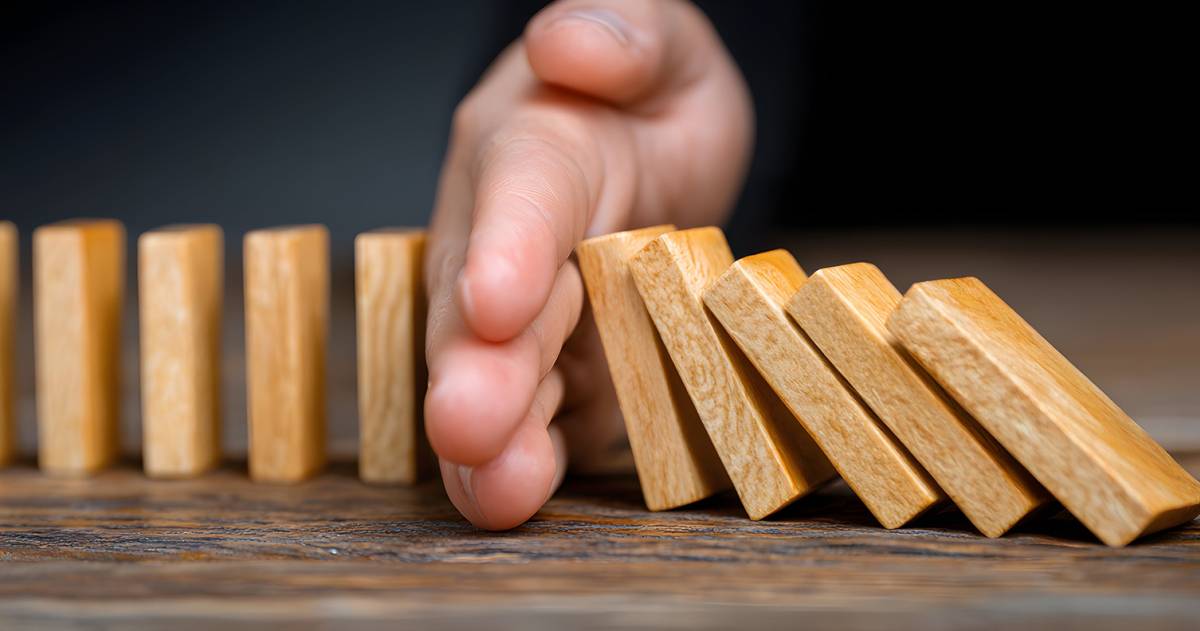 Een hand voorkomt een keting reactie van houten domino steentjes
